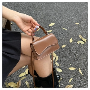 Détail d'un mini sac à main en cuir marron tenu sur fond de feuilles d'automne