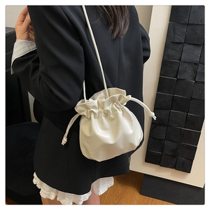 Dettaglio della borsa a secchiello color crema con coulisse indossata su un blazer