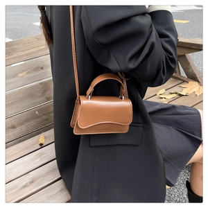 Close-up of brown mini handbag with wavy flap design worn by a model in park setting