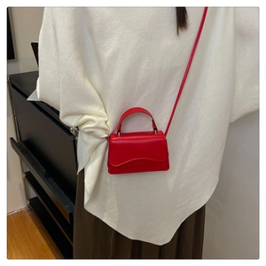 Detail of red mini crossbody bag with a unique wavy flap design and silver hardware accents