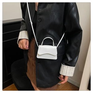 Gros plan du mini sac blanc en cuir avec rabat ondulé porté sur une veste noire