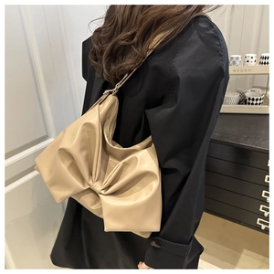 Detail of a beige shoulder bag with a large decorative bow and wide strap on a model