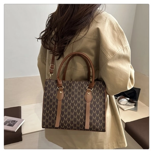 Brown monogram tote bag with M-pattern and leather straps shown on model in soft light