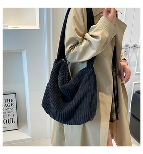 Model wearing a large black corduroy shoulder bag with casual textured crescent design