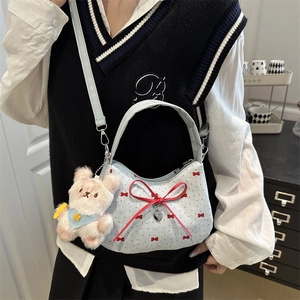 Blue canvas hobo bag with red bows and plush bear charm worn by a model in casual style