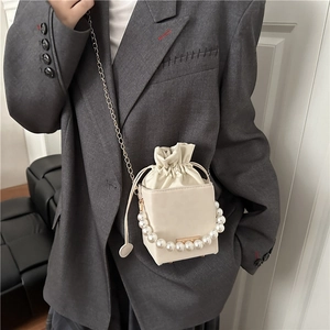 Chic cream drawstring bucket bag featuring a large pearl handle and gold chain strap