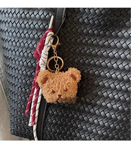 Vue détaillée d'un charm ours en peluche marron attaché à un sac cabas tressé noir