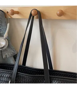 Détail d'un sac cabas noir tissé avec de longues bandoulières en cuir lisses