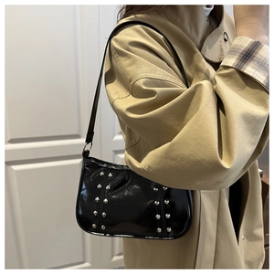 Détail du sac sous l'aisselle en cuir verni noir avec clous argentés sur un modèle