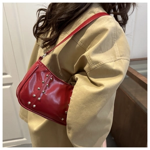 Détail du sac à bandoulière en cuir verni rouge avec clous argentés porté par le mannequin
