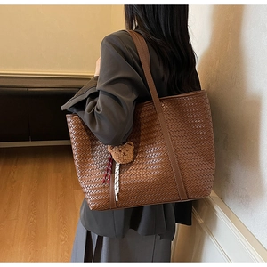Dettaglio borsa tote in pelle intrecciata marrone con ciondolo a orso su una modella