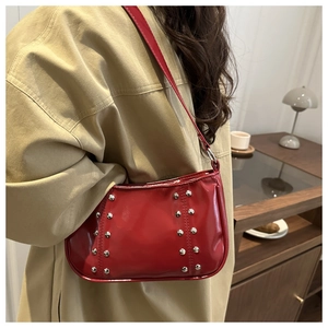 Detail of red glossy underarm bag with silver rivet accents on a beige trench coat