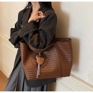 Détail d'un sac cabas tressé marron avec un charm ours en peluche et un gland à rayures
