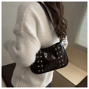 Détail du sac sous l'aisselle en cuir verni marron foncé avec rivets sur un modèle