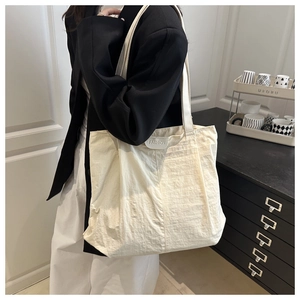 Detail of a cream white tote bag featuring soft pleated texture and fashion label