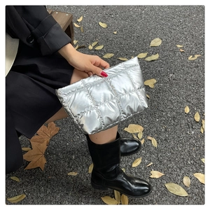 Gros plan d'une pochette matelassée argentée brillante tenue par un mannequin en extérieur