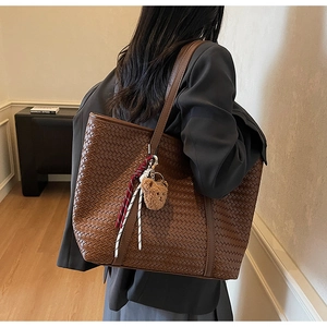 Dettaglio borsa tote intrecciata marrone con spalline sottili e ciondolo orsetto morbido