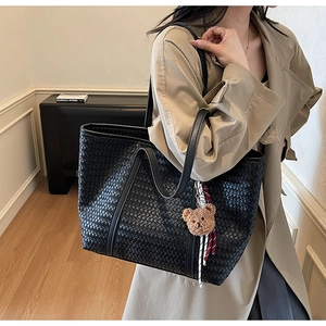 Dettaglio borsa shopper nera intrecciata con ciondolo a forma di orsetto e nastro a quadri