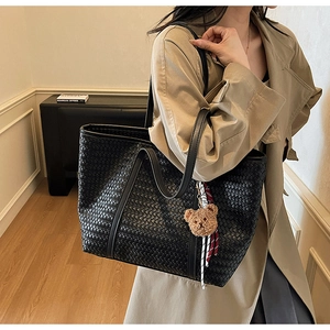 Dettaglio della borsa tote intrecciata nera con manico in pelle e ciondolo a forma di orso
