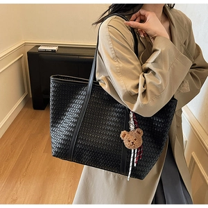 Dettaglio della borsa tote intrecciata nera con texture in pelle e ciondolo orso