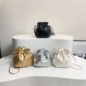 Mini drawstring bucket bags in black, gold, silver, and white on a minimalist stand