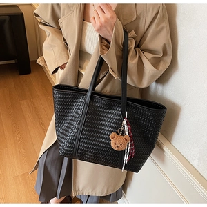 Dettaglio borsa tote intrecciata nera con ciondolo orsetto marrone e nastro a righe
