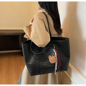Détail d'un grand sac cabas noir en cuir tressé avec pendentif ours sur un mannequin