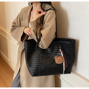 Dettaglio borsa tote intrecciata nera con ciondolo a forma di orsetto e nastro a righe