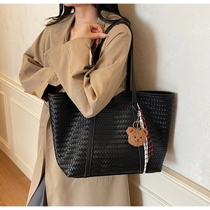 Dettaglio di una borsa tote nera intrecciata con ciondolo a forma di orso e nastro