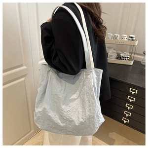 Detail of light blue wrinkled fabric tote bag with FASHION leather patch and woven strap