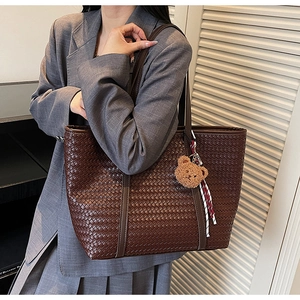 Détail d'un grand sac cabas tressé marron avec un porte-clés ours en peluche et ruban