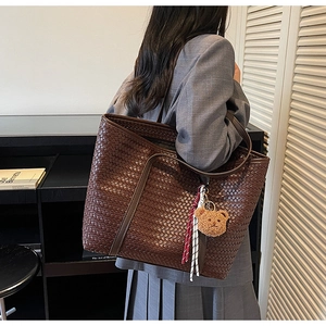 Dettaglio di una borsa tote intrecciata con sciarpa di seta e ciondolo a forma di orso