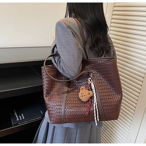Dettaglio di una borsa tote intrecciata marrone con ciondolo a orsetto sulla spalla