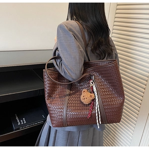 Dettaglio di una grande borsa tote intrecciata marrone con ciondolo a forma di orso