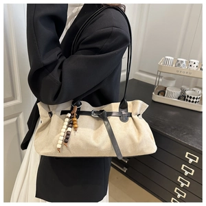 Detail of beige faux suede tote bag featuring black leather straps and beaded pendant charm