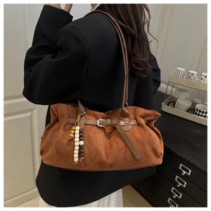 Detail of brown suede tote bag with leather strap buckle and beaded pendant accessory