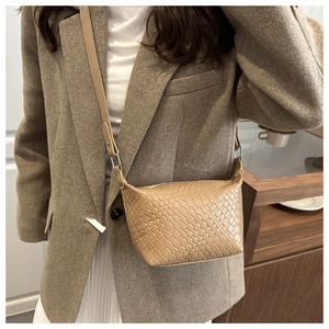 Detail of beige woven crossbody bag worn with brown blazer for office style
