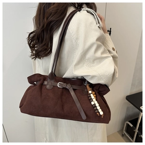 Detail of dark brown suede tote bag with leather buckle and beaded charm on white trench coat