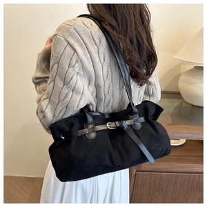 Detail of black suede shoulder bag with buckle strap on model in cozy interior