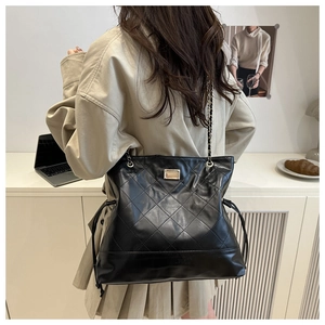 Quilted black tote bag with chain strap and drawstring detail shown on a model