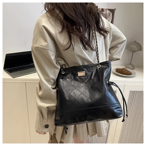 Detail of black quilted tote bag with chain strap shown in a modern lifestyle setting