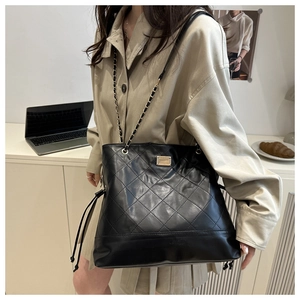 Detail of black quilted suede tote bag with metal chain strap and drawstring closure