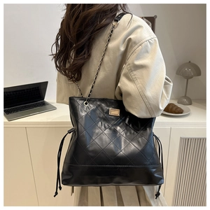 Detail of black quilted tote bag showing matte texture and elegant chain strap on shoulder