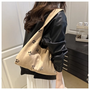 Detail of beige suede tote bag with flower cut-outs carried by a model in leather jacket