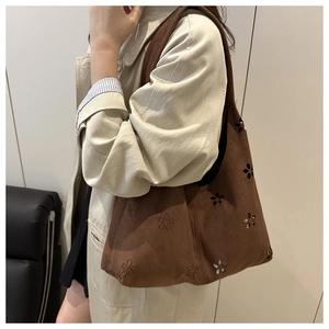 Detail of laser-cut floral patterns on brown suede shoulder bag with retro hollow design