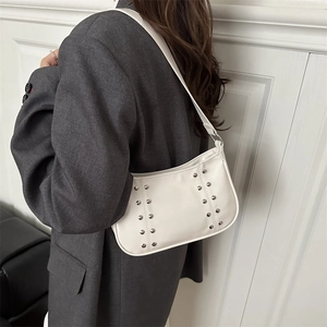 Sac hobo blanc élégant avec rivets argentés porté par un mannequin en costume gris chic