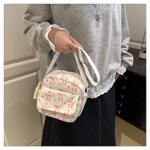 Détail du sac bandoulière en velours blanc avec nœuds roses et pompon beige