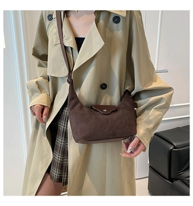 Model wearing a brown suede hobo bag with a crescent shape and metal magnetic closure