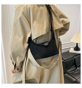 Detail of black suede crescent underarm bag with silver magnetic snap on trench coat