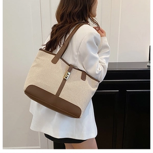 Detail of canvas tote bag with brown leather trim and golden metal swivel lock closure